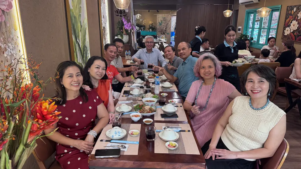 Bàn tiệc với các món ăn, mọi người ngồi hai bên cười tươi