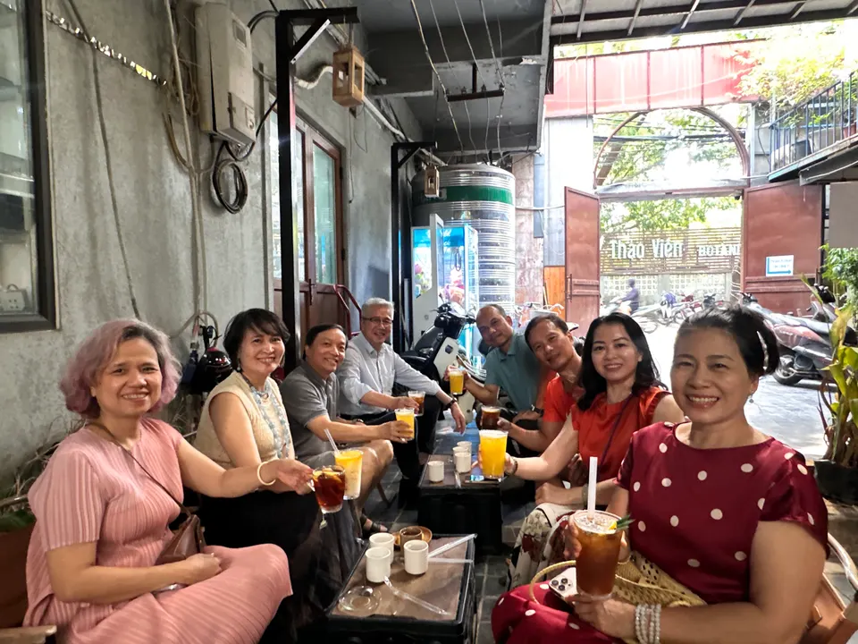 Cả nhóm ngồi quanh bàn nước nhỏ, cầm cốc trà đá và nước cam